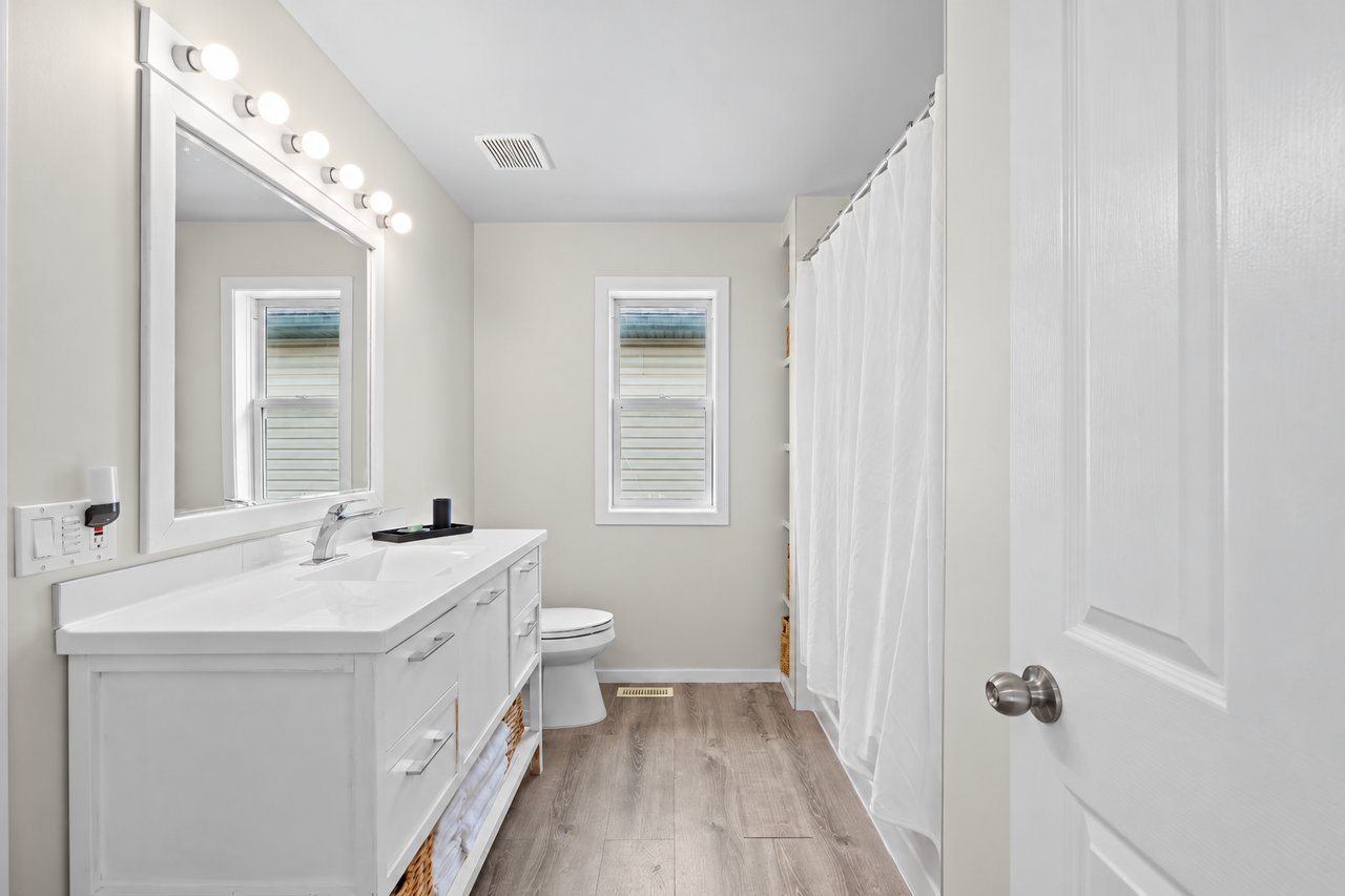 Bathroom with a long white vanity, large mirror, and window above the toilet.