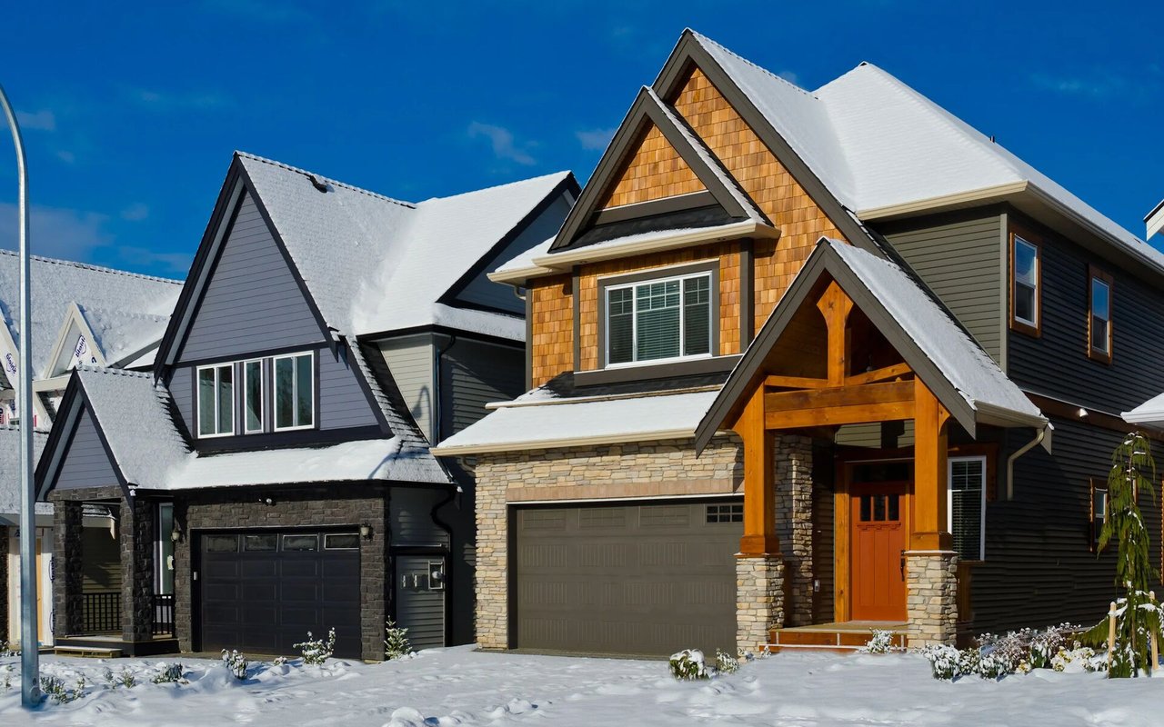 Two-story house with cedar-shingle gables, stone facade, timber entry porch, and snow-covered roof and yard.