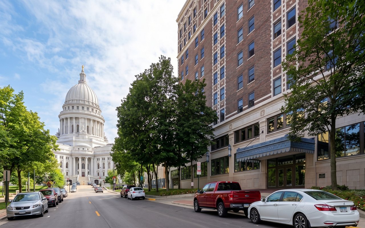 Multistory brick building beside a tree-lined street, with the Wisconsin State Capitol dome in the distance.