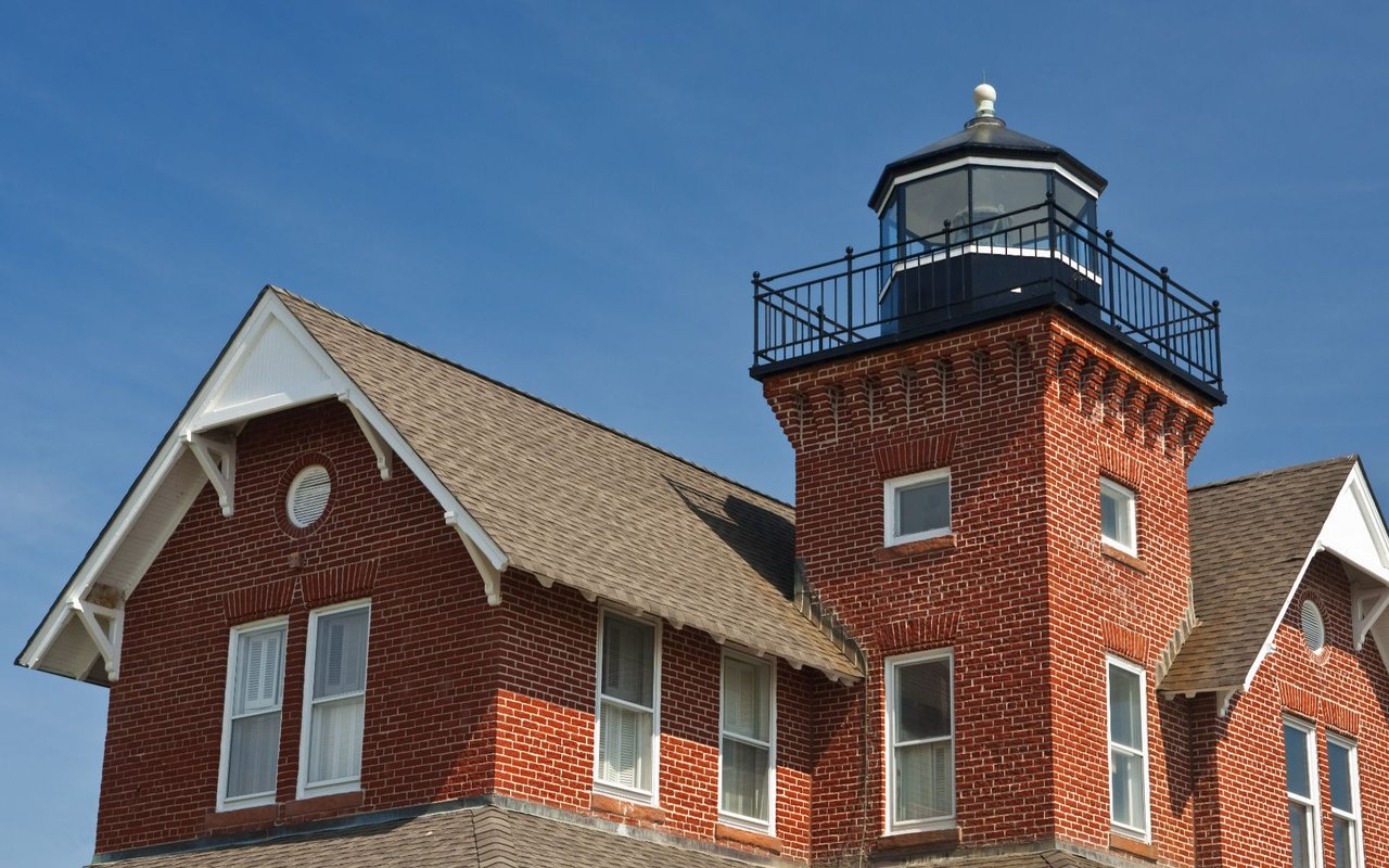 Sea Girt Lighthouse’s red-brick tower and black lantern room against a clear blue sky.
