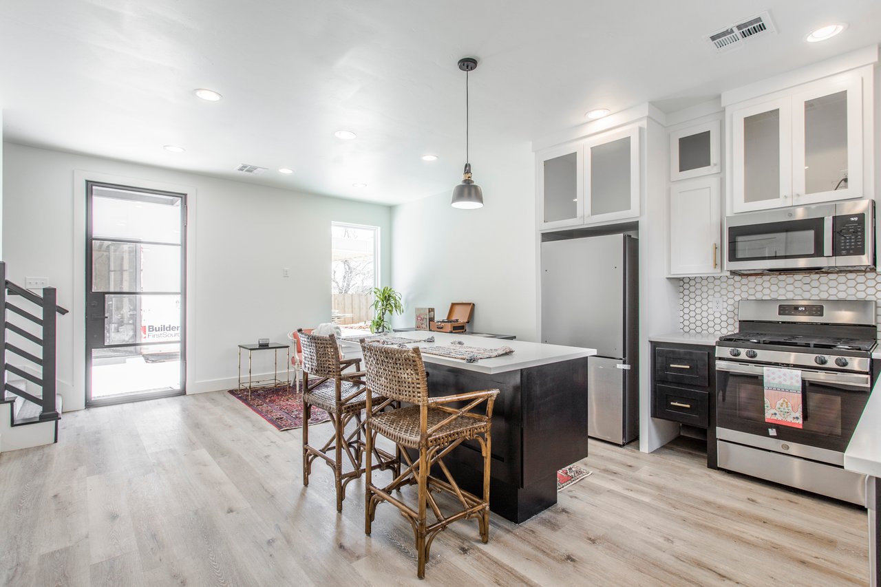 Open kitchen with a large black island, woven bar stools, and stainless steel appliances.
