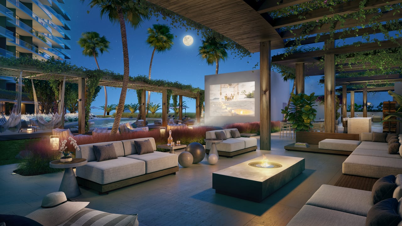 Outdoor lounge terrace with sofas, fire pit, palms, and a glimpse of water at night.
