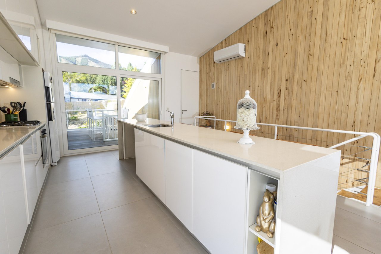 Modern kitchen with a long white island, wood-paneled wall, and patio doors facing a mountain view.