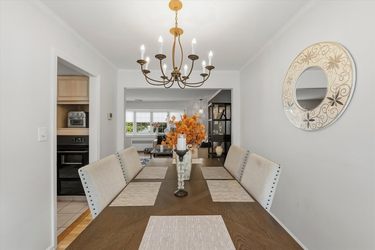 Dining room with a long wood table, upholstered chairs, and a chandelier, opening to adjoining living spaces.
