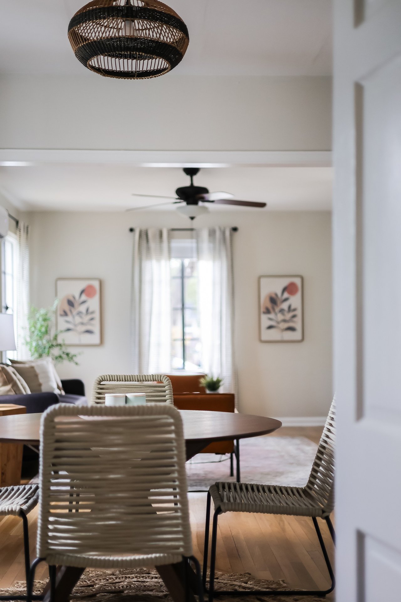 Dining area with a round wood table, woven chairs, and pendant light opening into a bright living room.