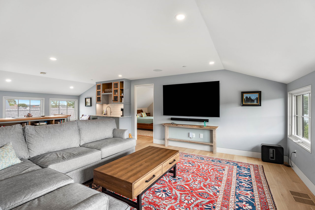 Living room with a gray sectional, patterned red rug, wall-mounted TV, and built-in bar.