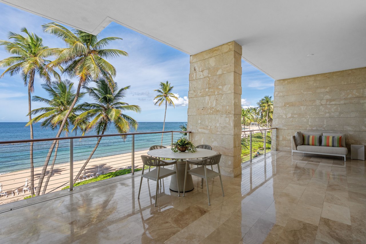 Covered beachfront terrace with a dining table, palm trees, and ocean views.