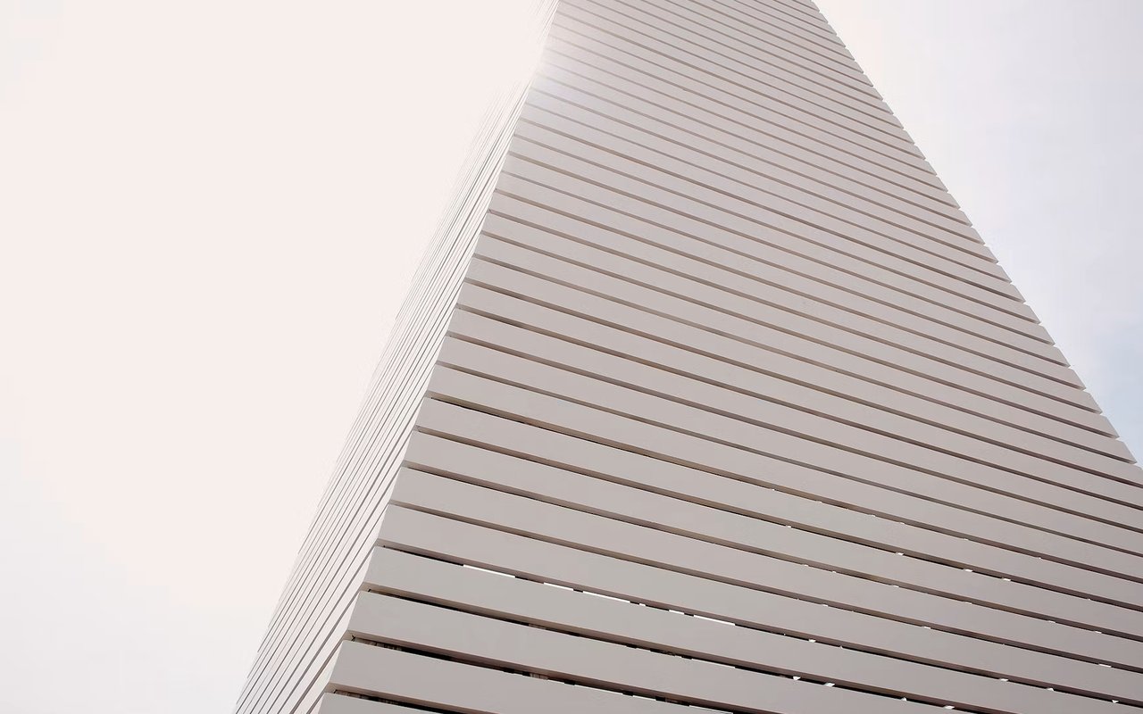 Modern building facade viewed upward, with repeating horizontal bands against a pale sky.