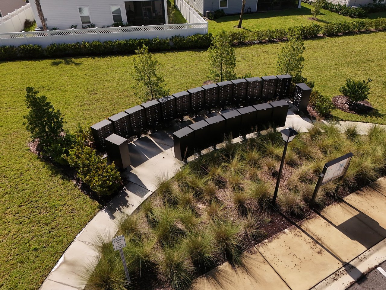 Community mailboxes beside a landscaped walkway, with homes and lawns nearby.