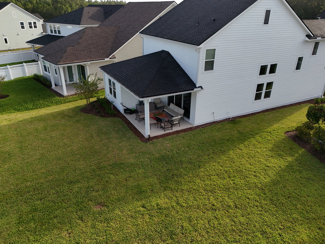 Rear of a white two-story home with a furnished covered patio and broad green lawn.