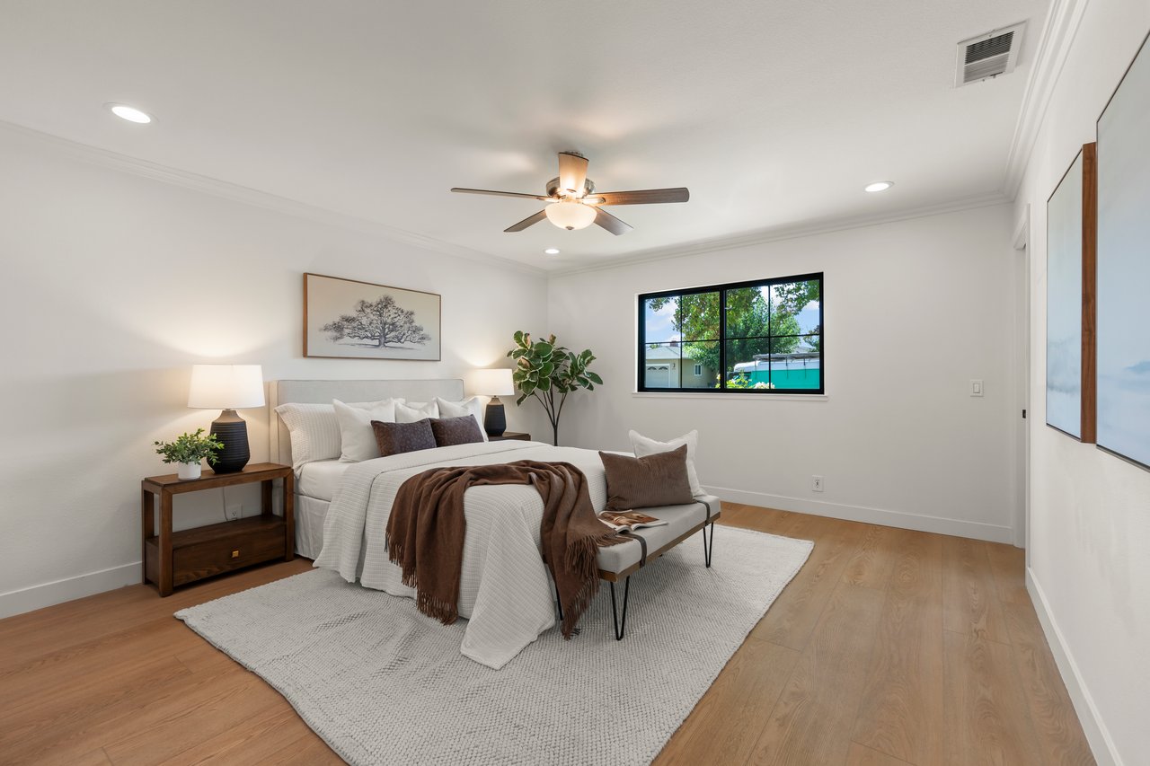 Staged bedroom with a white bed, brown throw, ceiling fan, and large black-framed window.