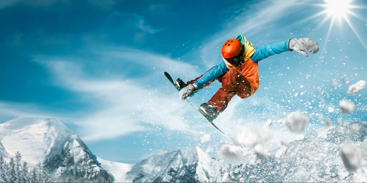 Skier jumps through powder on a sunny mountain slope.