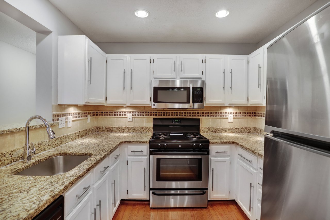 Kitchen with white cabinetry, granite counters, stainless appliances, and hardwood floors.