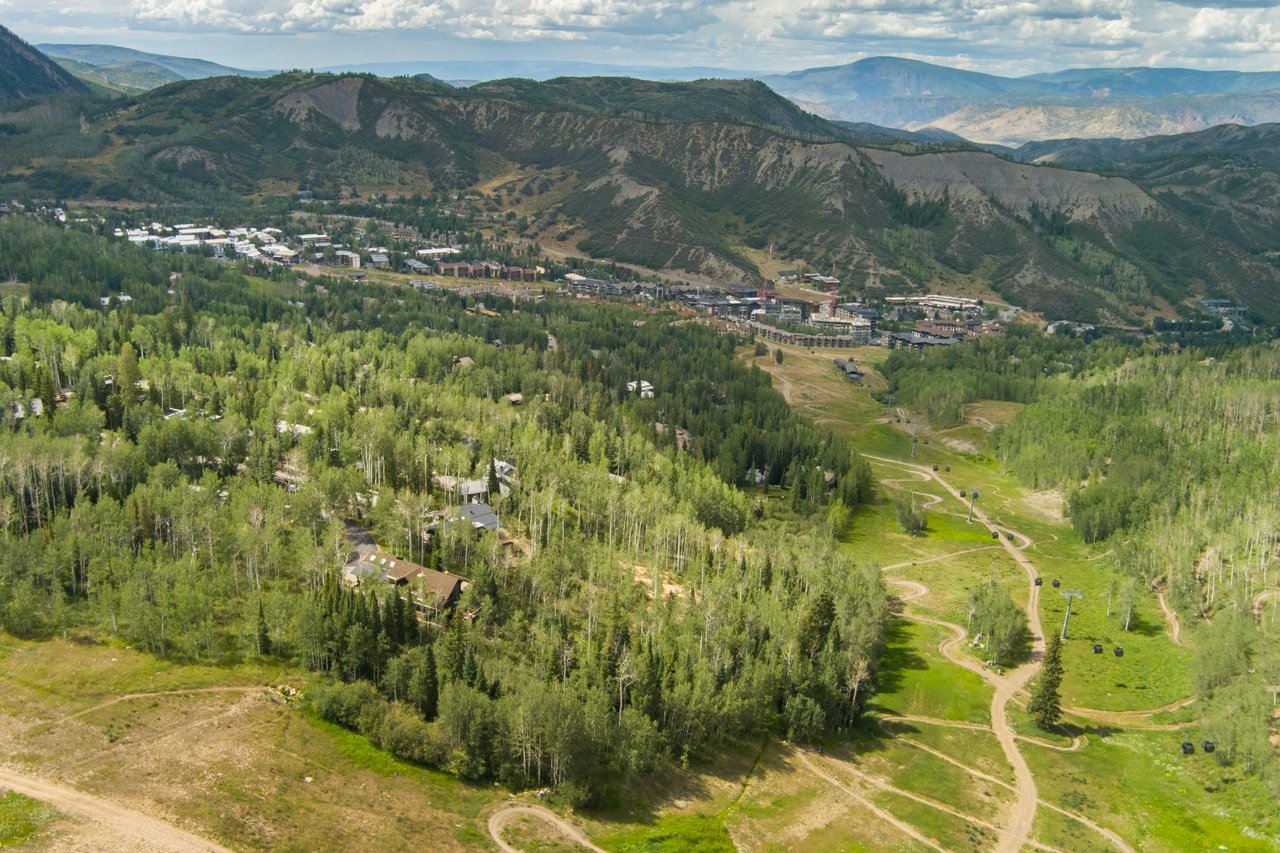 Aerial view across Snowmass ski slopes, lift lines, resort buildings, and surrounding mountains.