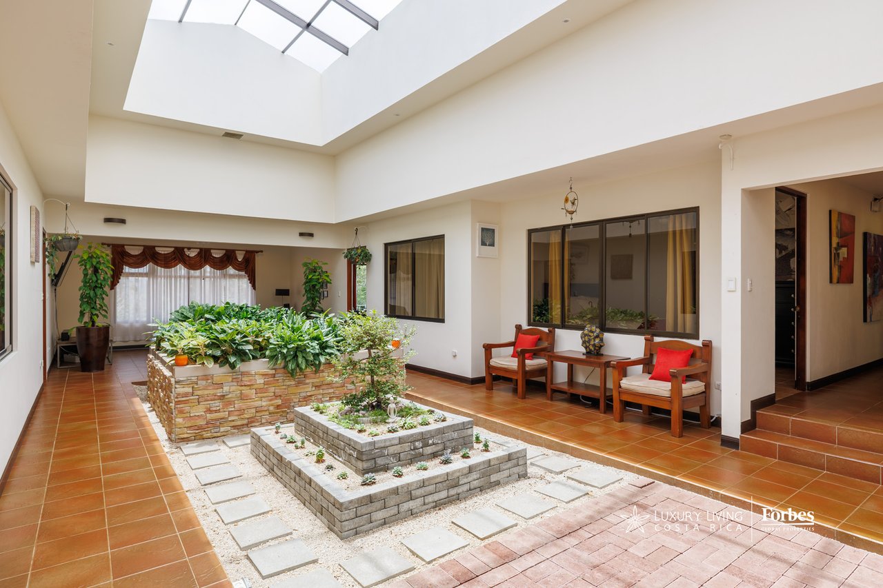 Interior atrium with a skylight, planted stone beds, tiled floors, and wooden seating.