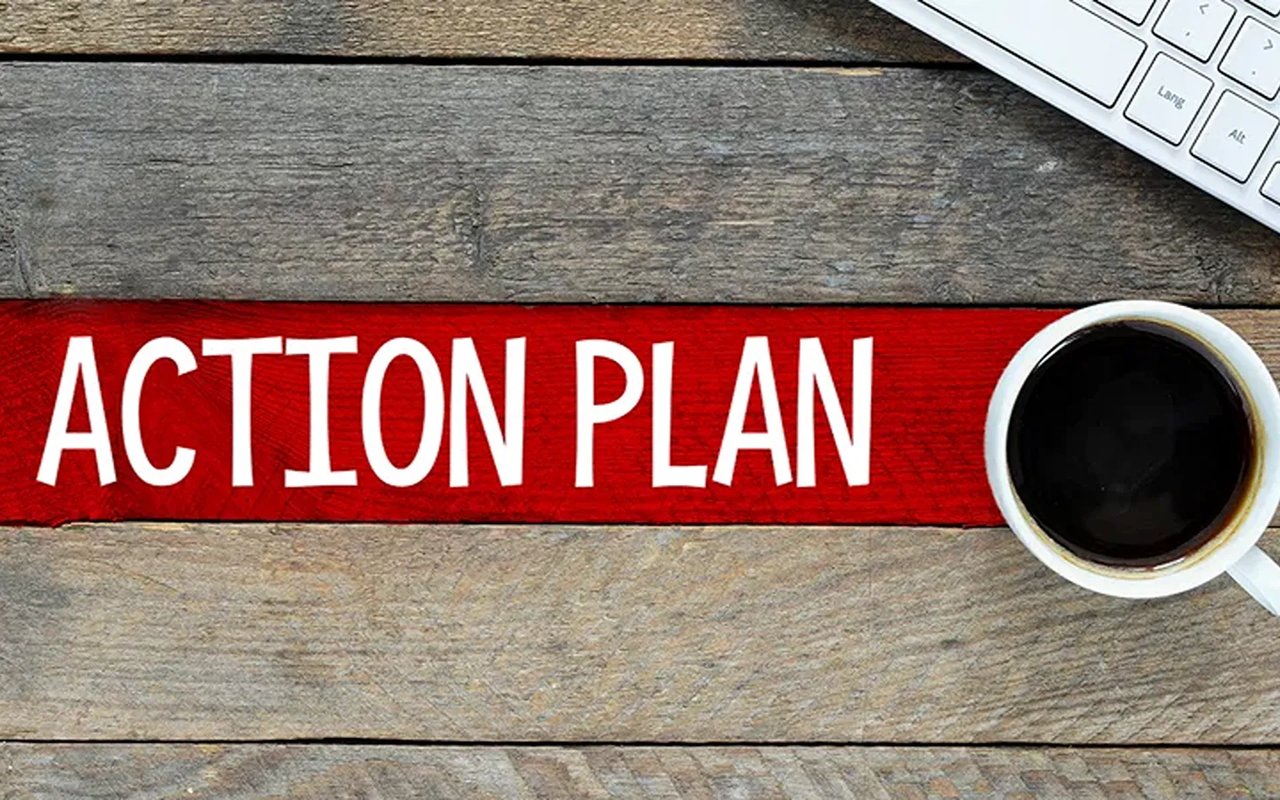 Action plan written on a red strip beside coffee and part of a keyboard.