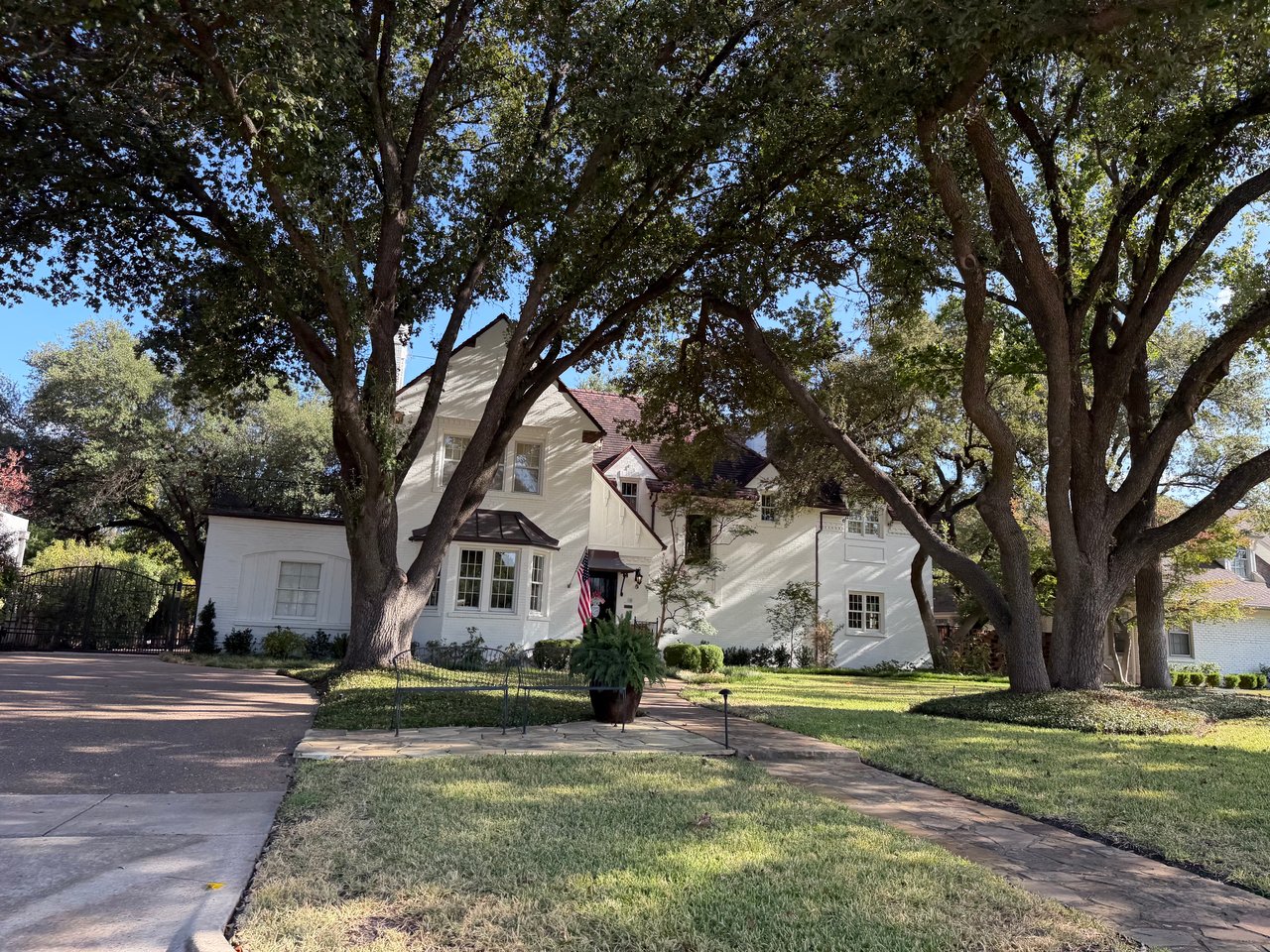 White two-story house framed by mature trees, with a broad driveway and stone walkway.