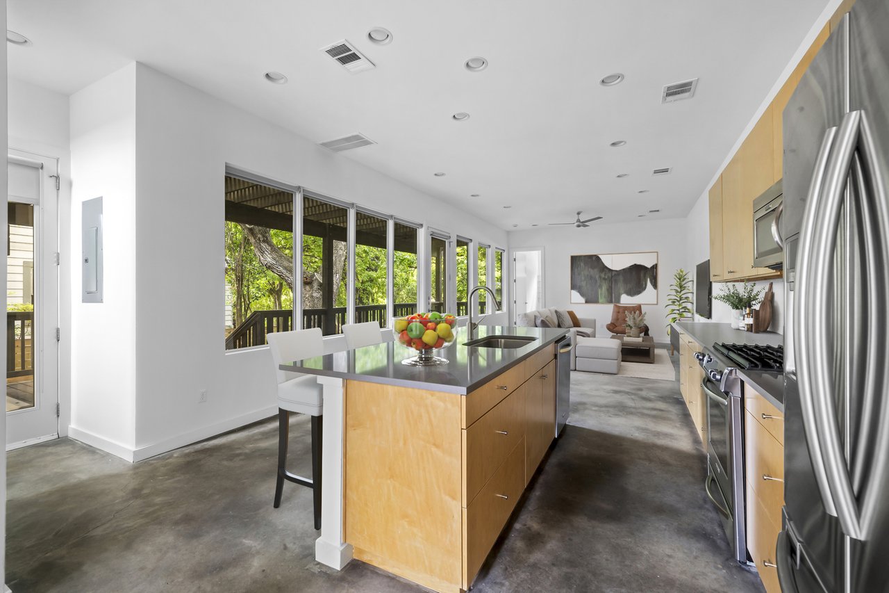 Chef's kitchen at 1302 S 5th St Unit A, Bouldin, Austin, TX, with a wood island, stainless appliances, concrete floors, and a wall of windows to the screened porch and trees.