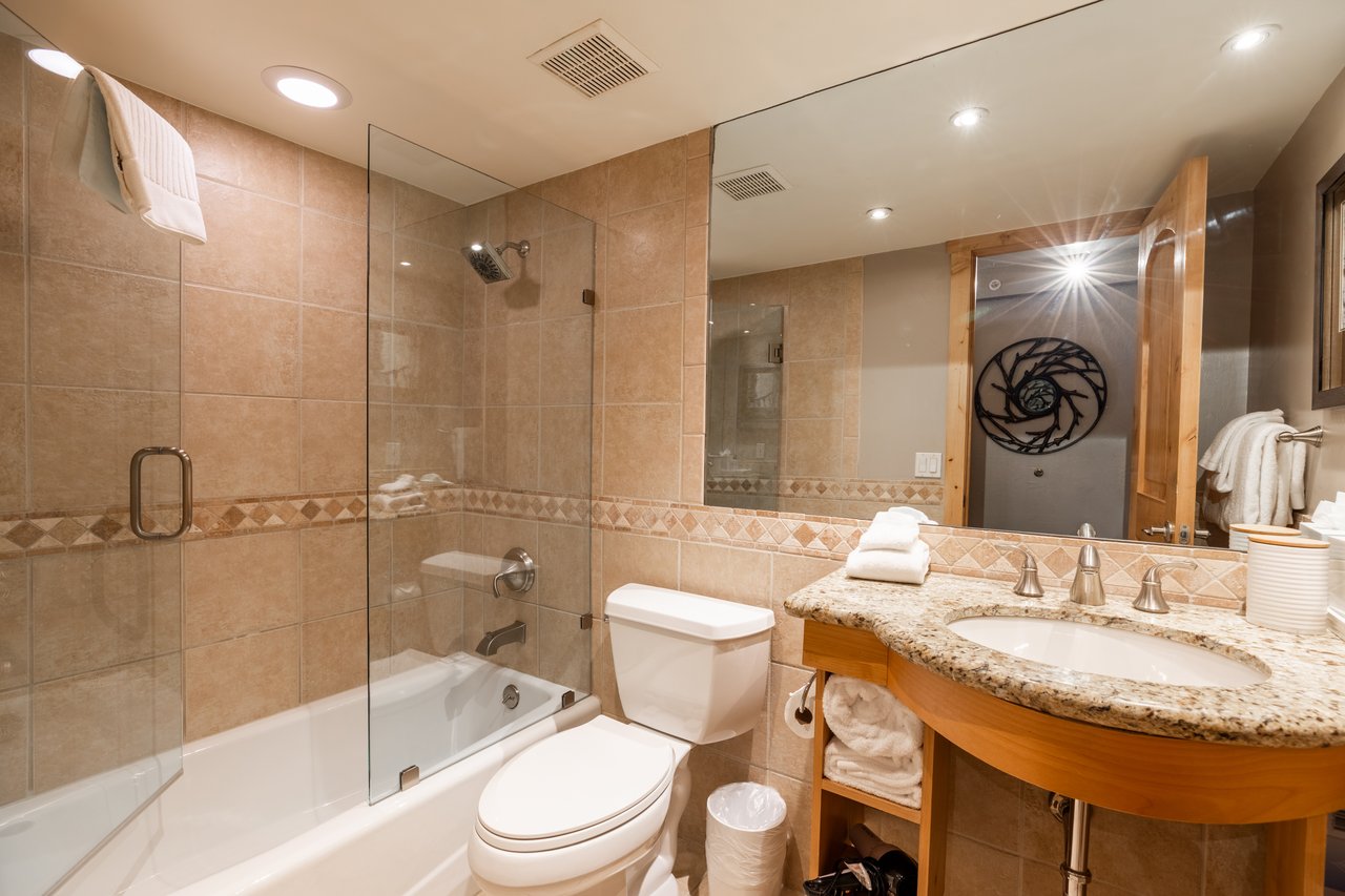 Bathroom with a glass-enclosed tub, tan tile, and granite-topped wood vanity.