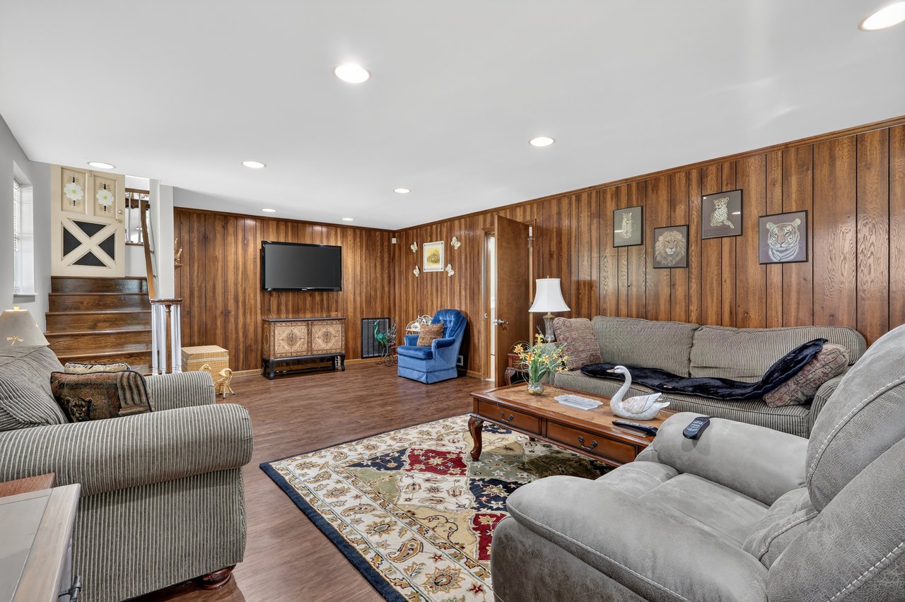 Living room with wood-paneled walls, a staircase, and seating around a patterned rug.