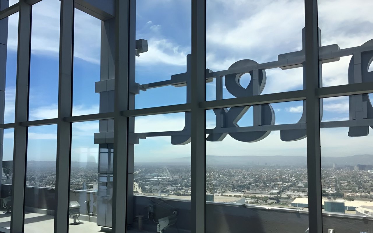 Downtown Los Angeles skyline seen through floor-to-ceiling windows with exterior lettering in the foreground.