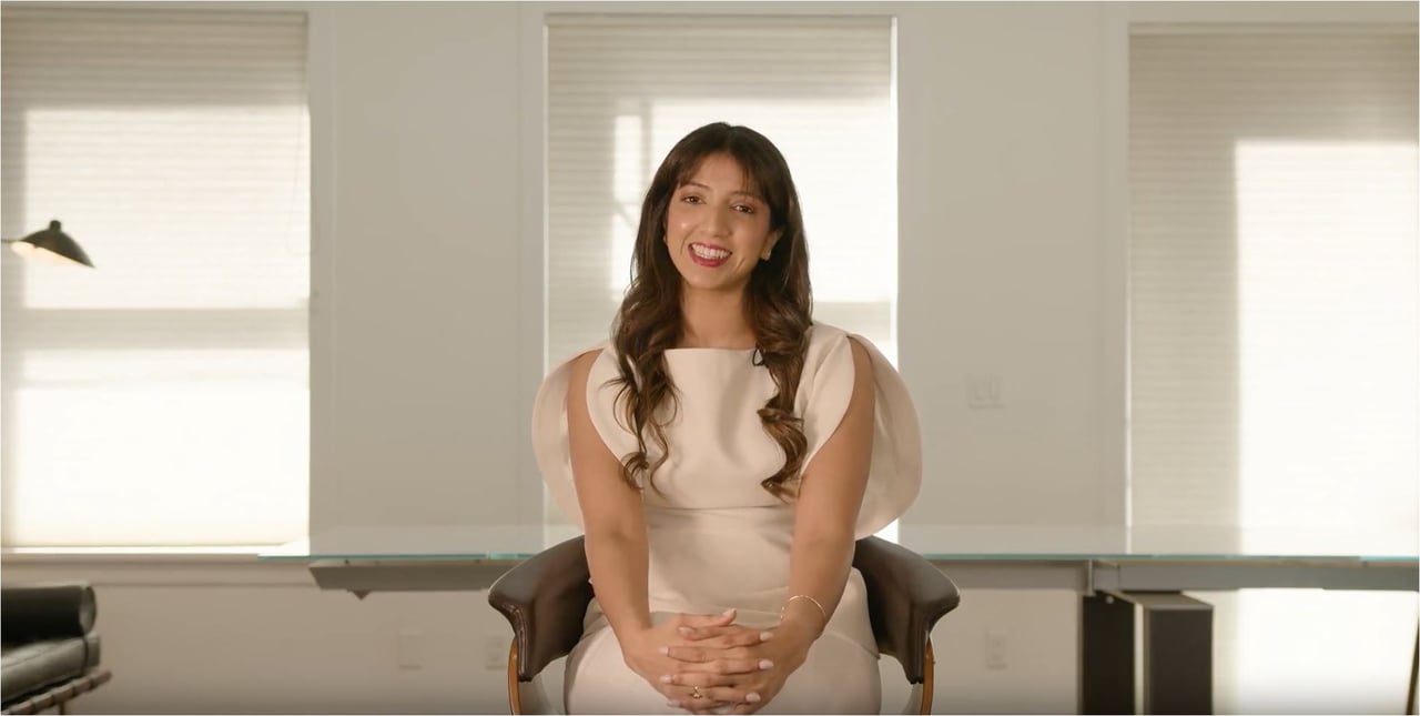Neha Vernekar seated in a chair in a bright office, wearing a white dress.