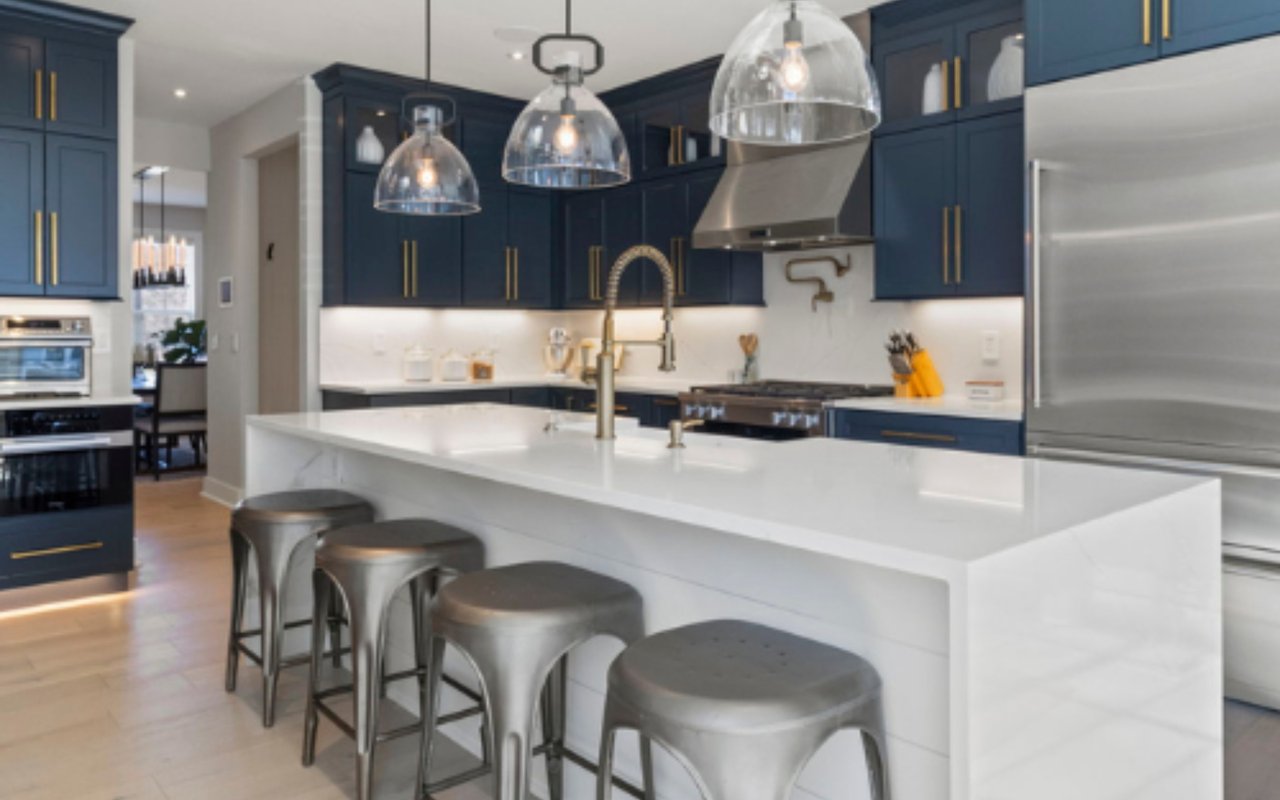 Modern kitchen with navy cabinets, a large white island, brass fixtures, and metal bar stools.