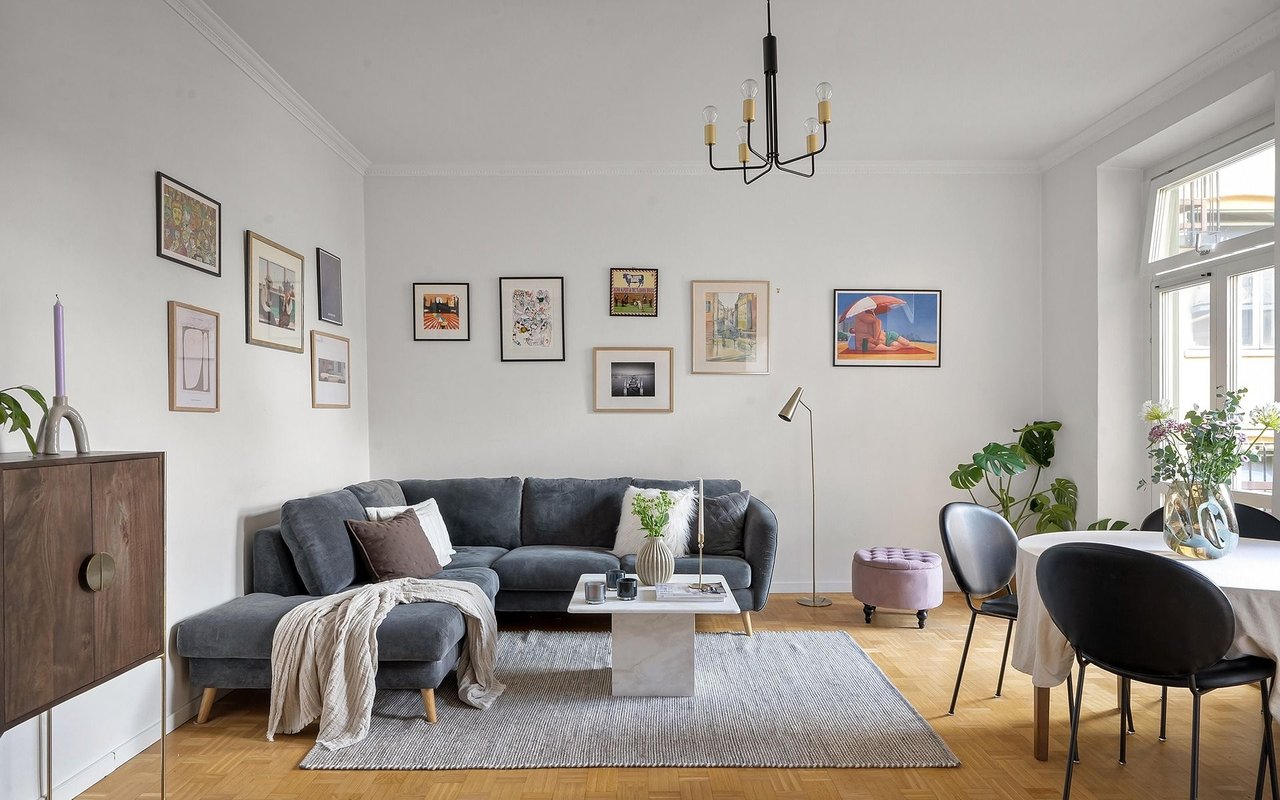 Living room with a dark gray sectional, framed art, parquet floors, and dining area by large windows.