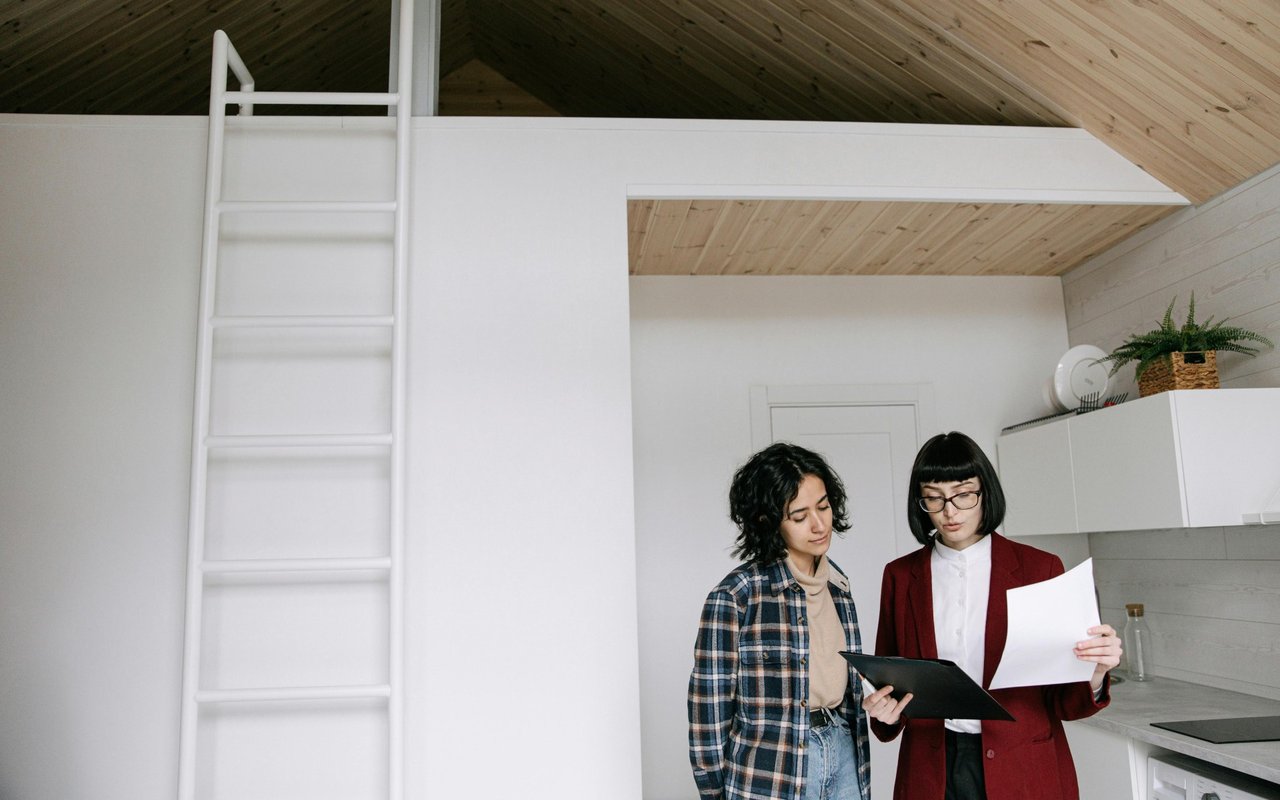 Two women review paperwork in a compact kitchen with a ladder to the loft.