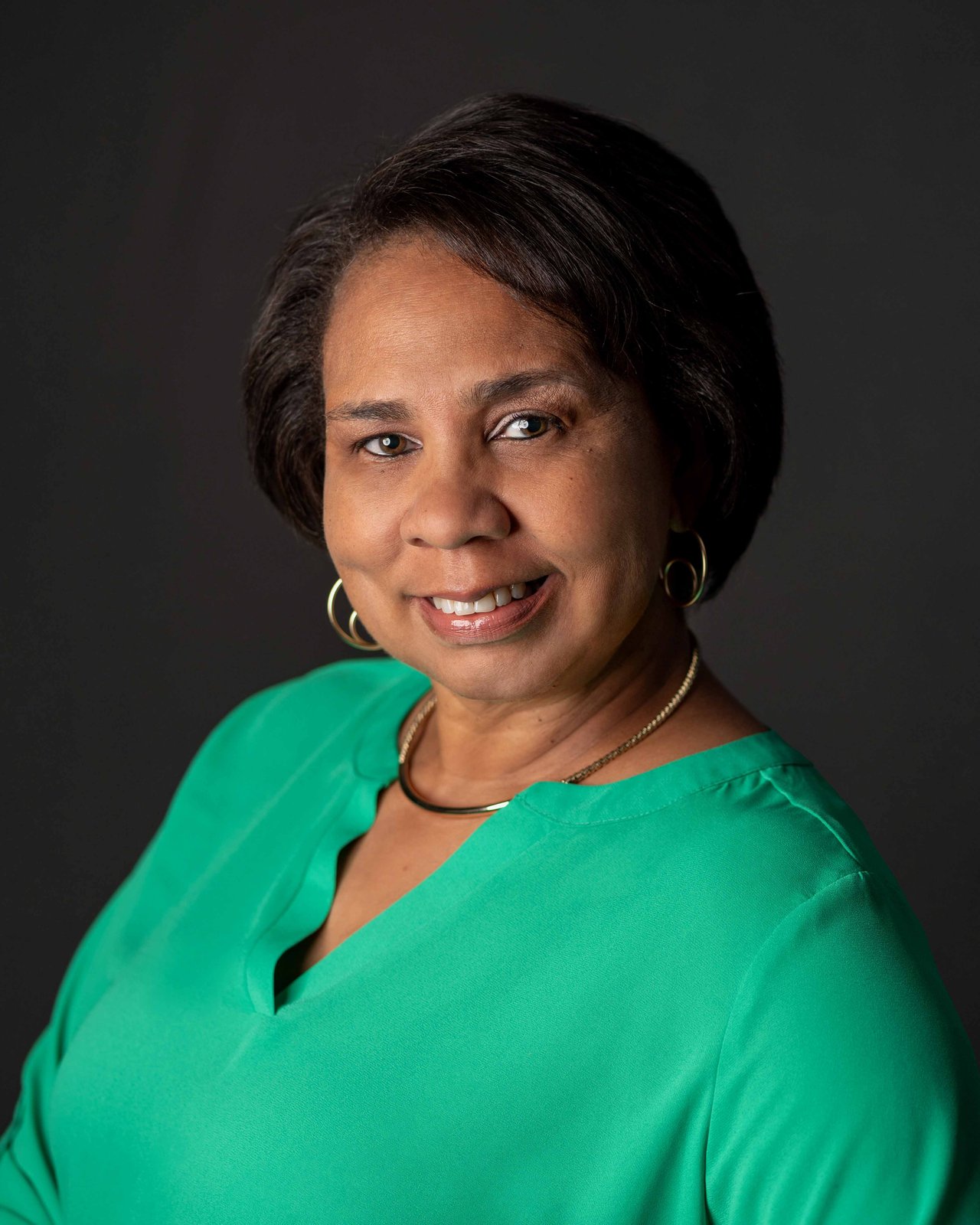 Vickie Scotland smiling in a bright green blouse against a dark background.