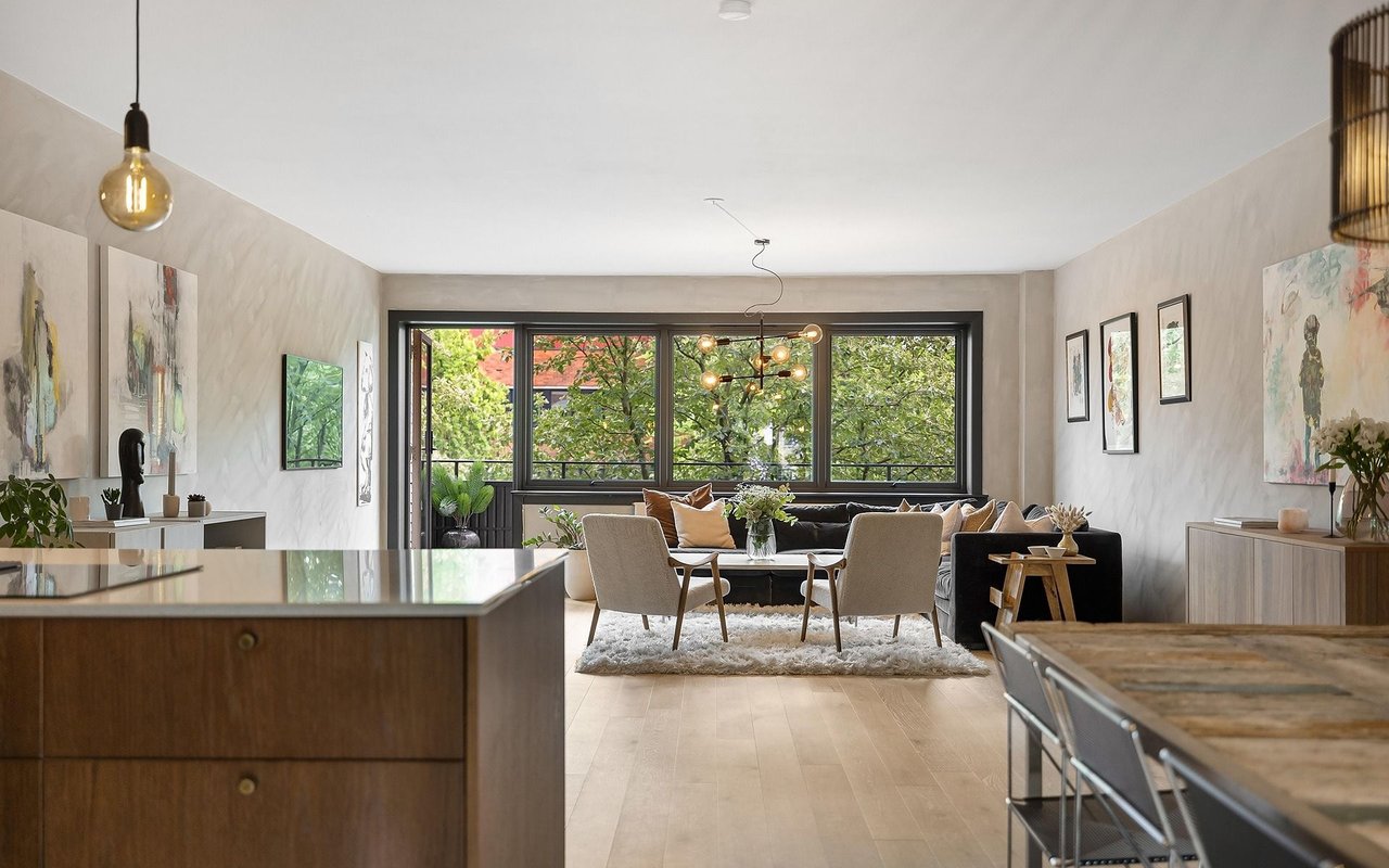 Open-plan living room with a dark sofa, dining table, and large windows overlooking trees.