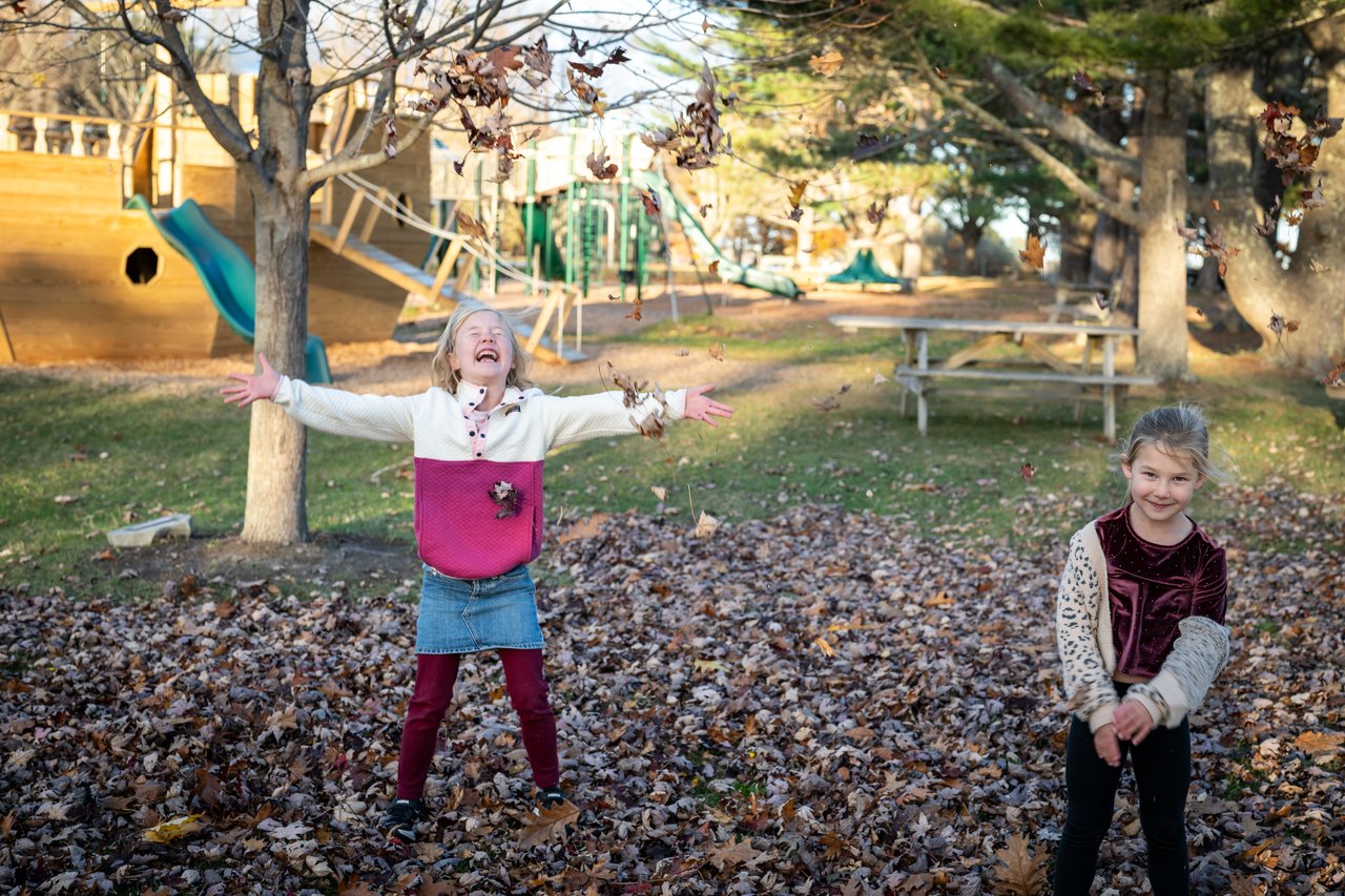 Two children play among fallen leaves at a playground in autumn.