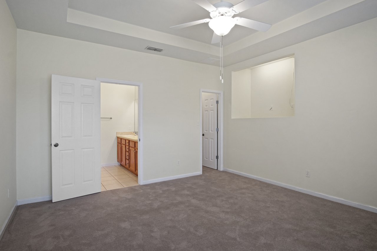 Primary bedroom at 5441 Hampton Hill Circle, Tallahassee, Florida 32311 featuring tray ceiling, ceiling fan, and doorway to ensuite bathroom.