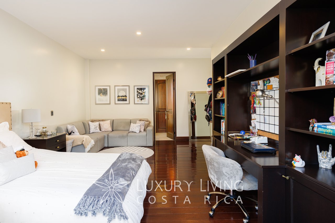 Bedroom with a white bed, gray sitting area, dark built-in shelving, and polished wood floors.