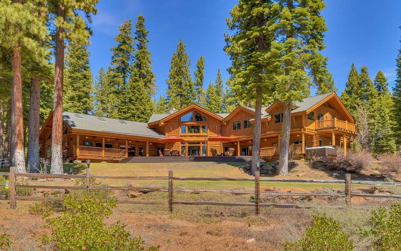 Large timber lodge with broad decks and a hot tub among tall pines.