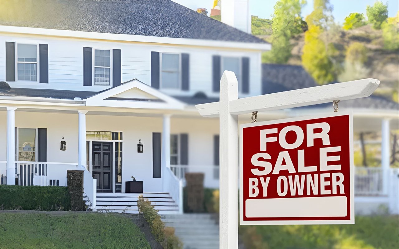 White two-story house behind a prominent For Sale By Owner sign.
