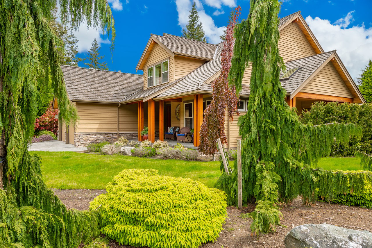 Tan multi-gabled home with a covered porch, stone accents, and a lush landscaped yard.