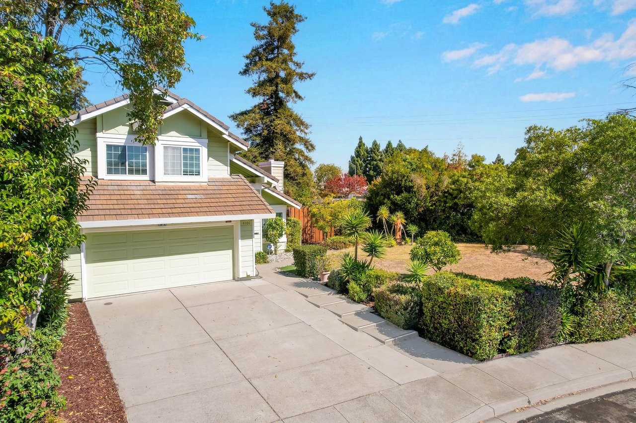 Light green house with a two-car garage, broad driveway, and landscaped front yard.