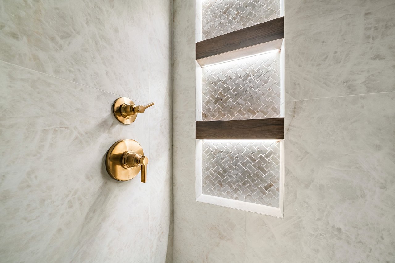 Shower with gold controls and a geometric-tile niche with dark wood shelves.