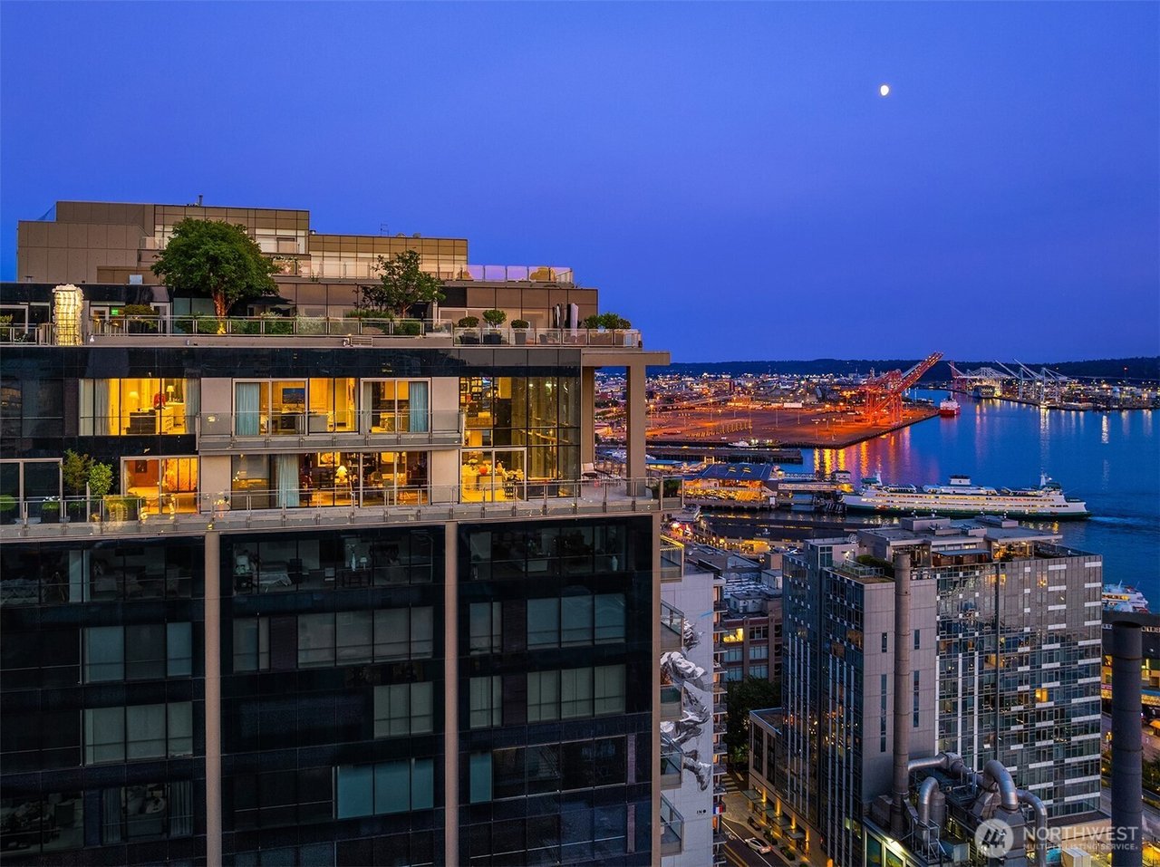 Modern Seattle waterfront condominium at dusk, with rooftop terraces and illuminated windows overlooking the harbor.