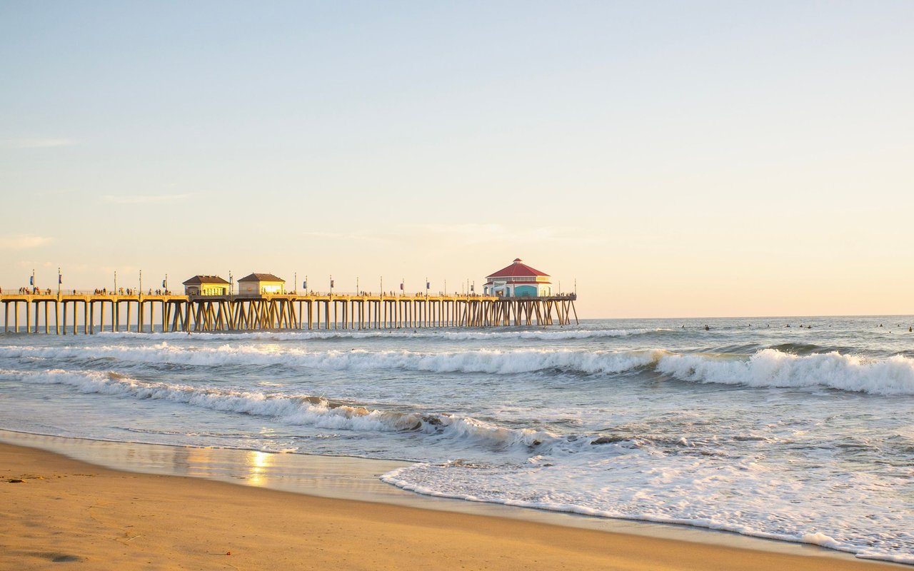 Huntington Beach pier stretches over the ocean as waves break along the sunlit shore.