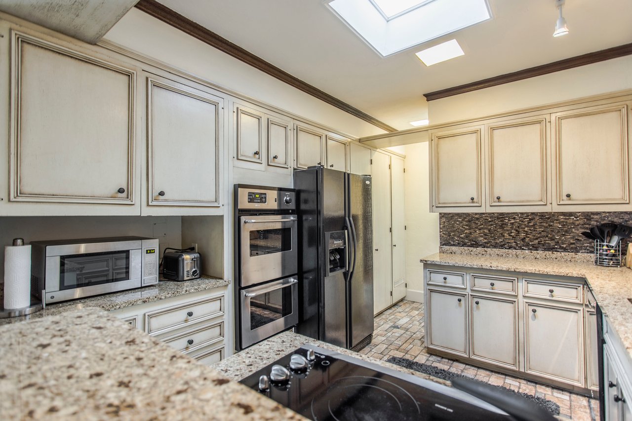 Kitchen with cream paneled cabinets, granite counters, stainless steel double ovens, and a skylight.