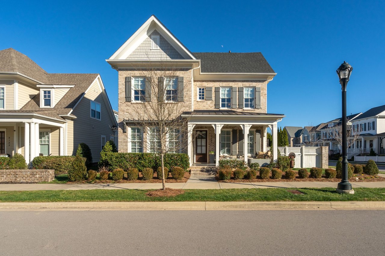 Two-story brick-and-stone house with a front porch, gabled roof, and landscaped yard on a residential street.