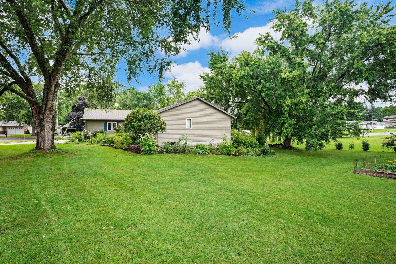 A single-story home set on a large open lawn framed by mature trees, the kind of property outside the city that relies on a private well and septic.