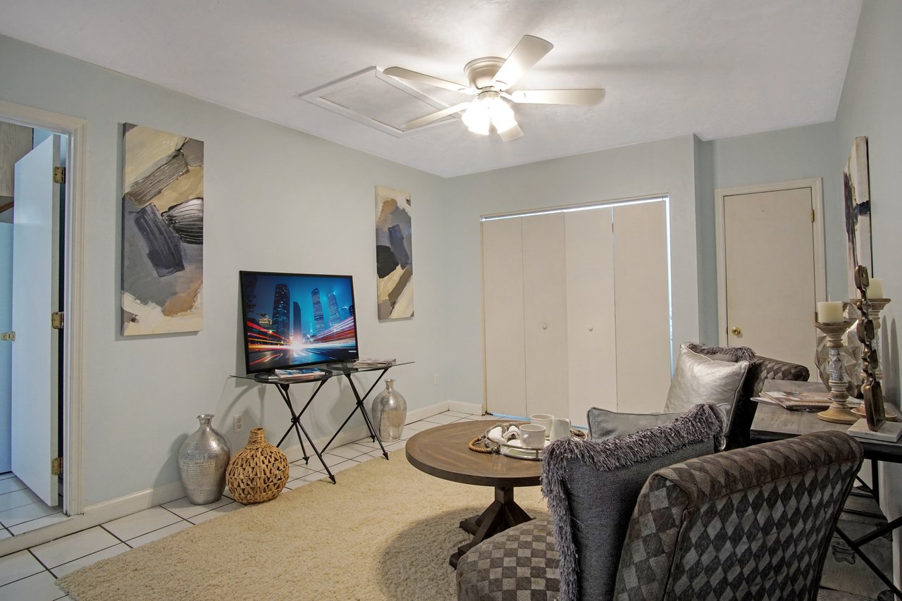 Cozy living room with a TV on a stand displaying a cityscape. Neutral tones, abstract art, modern chairs, coffee table with cups, and soft lighting add warmth.Cozy living room with a TV on a stand displaying a cityscape. Neutral tones, abstract art, modern chairs, coffee table with cups, and soft lighting add warmth.