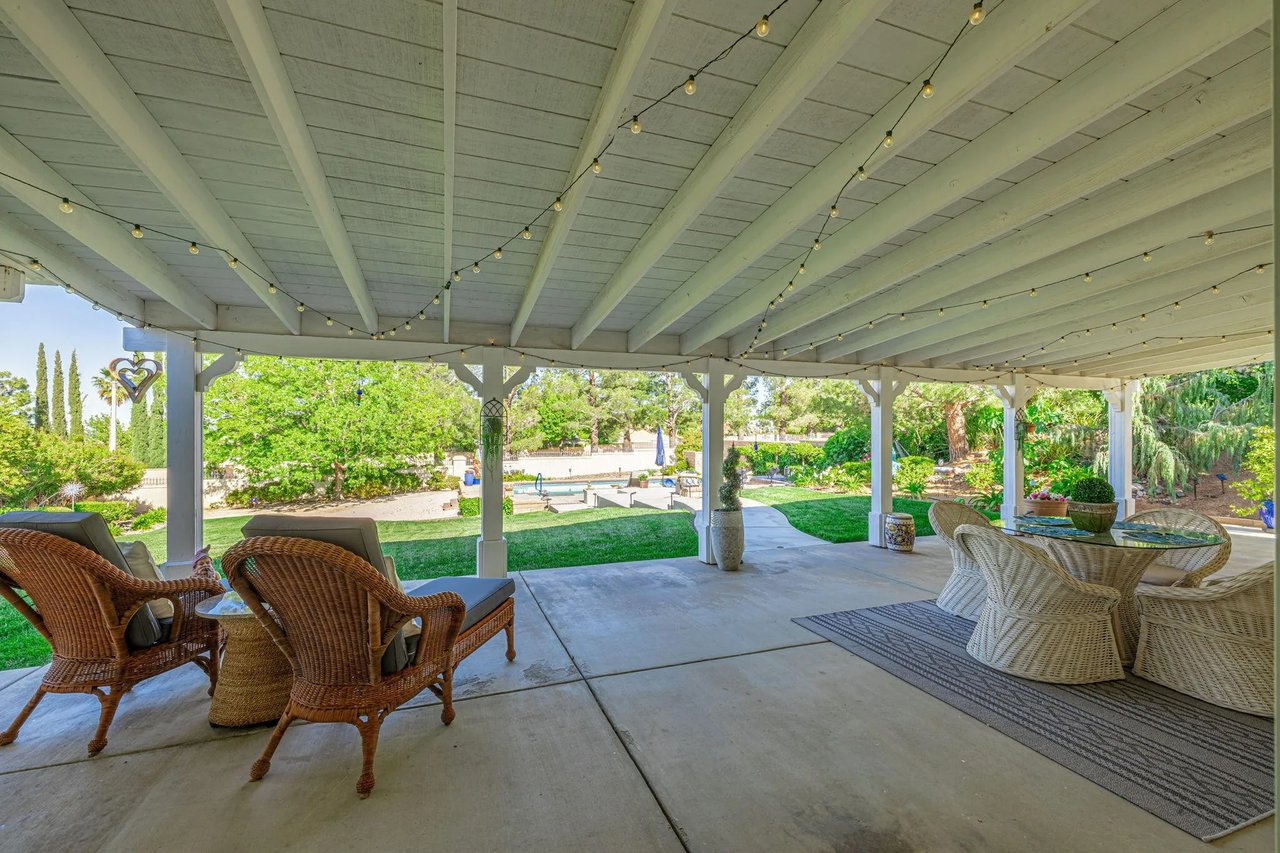 Covered patio with string lights, wicker seating, and a view of the pool and landscaped yard.