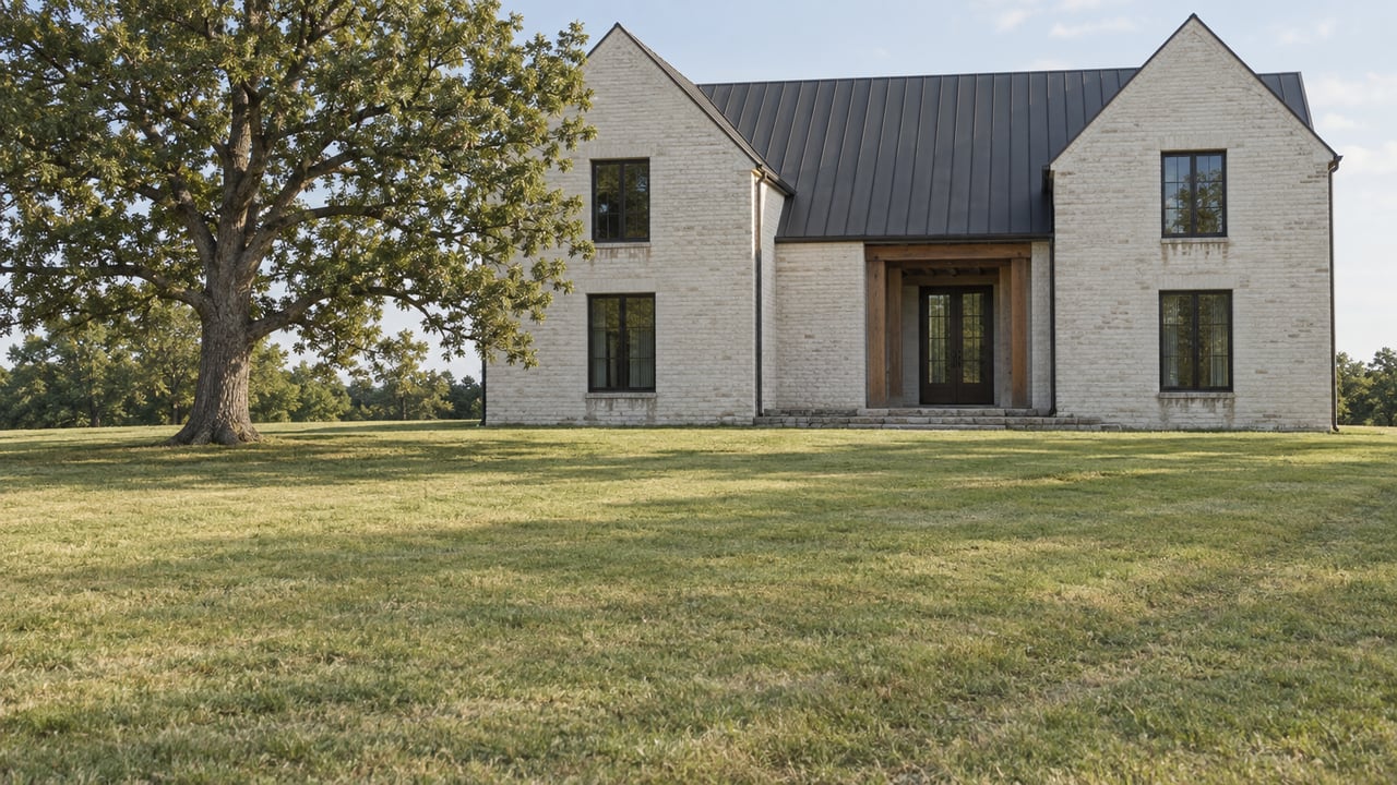 A two-story off-white brick house sits beyond a broad lawn, with a mature oak tree to the left.