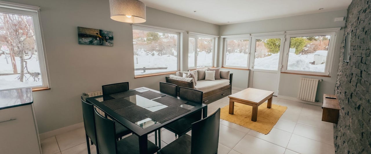 Living and dining area with a black table, sofa, and windows overlooking snow.