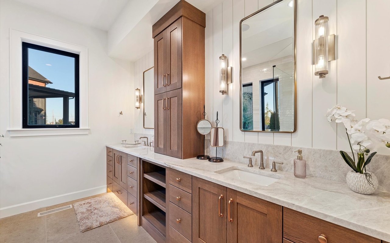 Primary ensuite bathroom with dual vanities, brass and nickel hardware, and custom wood cabinets
