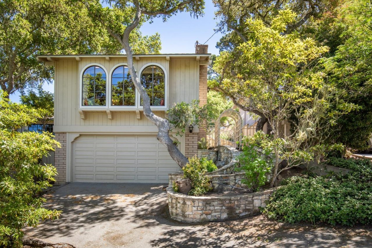 Home with three arched windows, an attached garage, and a curved stone retaining wall.